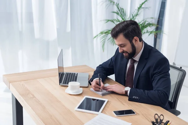 Side view of businessman making notes in notebook at workplace in office — Stock Photo