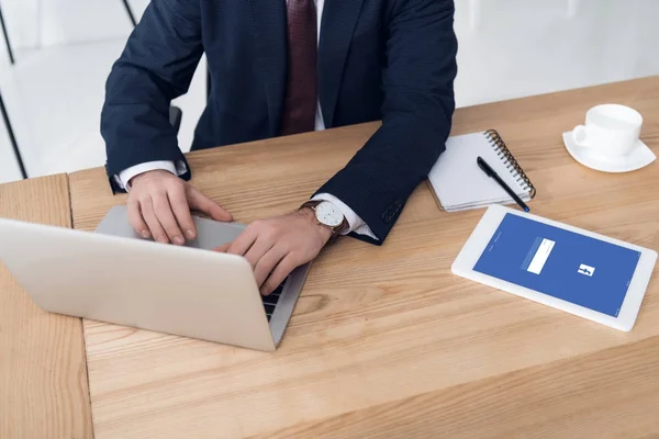 Vista parcial del empresario que trabaja en el ordenador portátil en el lugar de trabajo con la tableta en la oficina - foto de stock