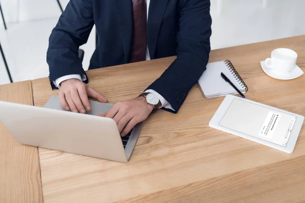 Vista parcial del empresario que trabaja en el ordenador portátil en el lugar de trabajo con la tableta en la oficina - foto de stock
