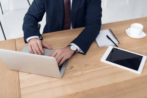 Vista parcial del empresario que trabaja en el ordenador portátil en el lugar de trabajo con la tableta en la oficina - foto de stock