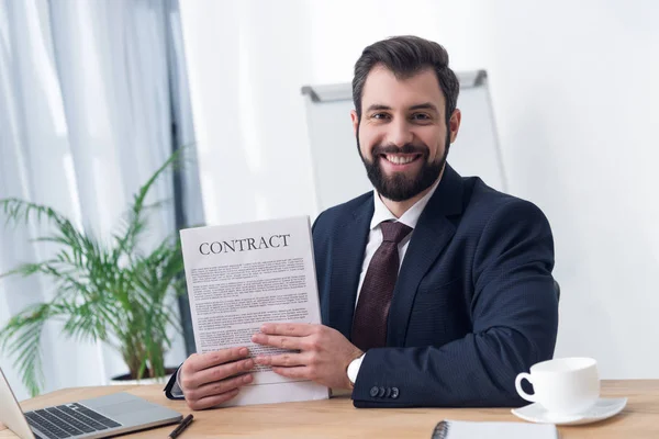 Portrait of smiling businessman with contract at workplace in office — Stock Photo