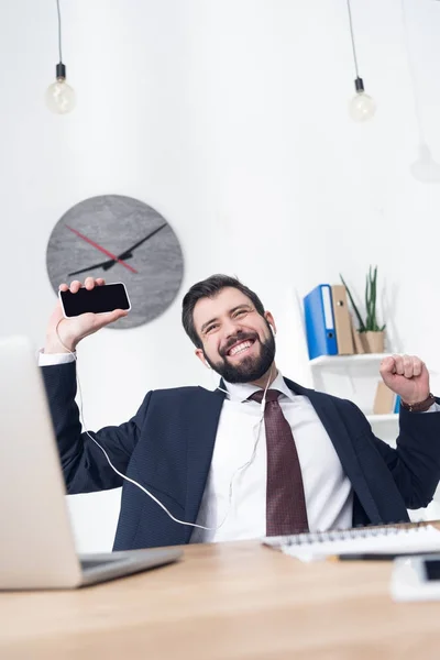 Бизнесмен слушает музыку в наушниках со смартфоном на рабочем месте в офисе — стоковое фото
