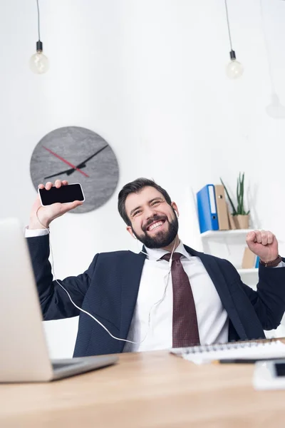 Businessman listening music in earphones with smartphone at workplace in office — Stock Photo