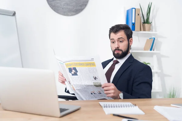 Portrait of emotional businessman in suit reading newspaper at workplace in office — Stock Photo