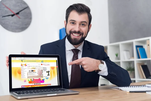 Портрет улыбающегося бизнесмена, указывающего на ноутбук на рабочем месте в офисе — стоковое фото