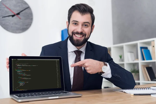 Portrait of smiling businessman pointing at laptop at table in office — Stock Photo