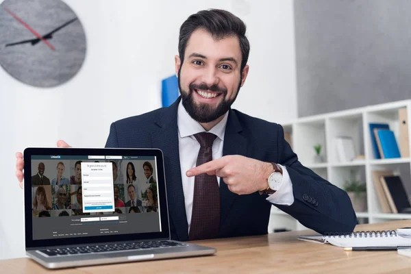 Portrait of young businessman pointing at laptop at workplace in office — Stock Photo