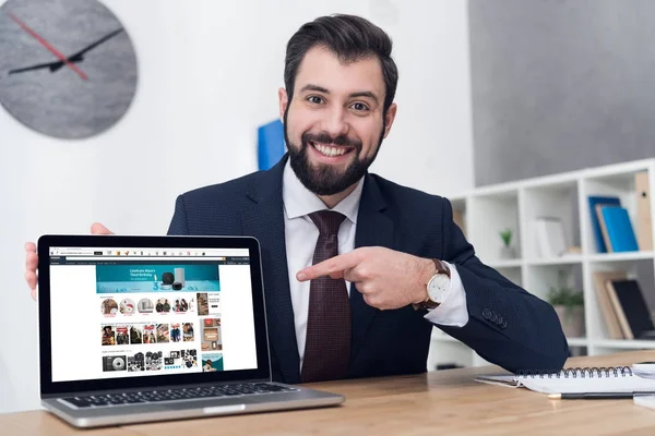 Portrait of young businessman pointing at laptop at workplace in office — Stock Photo