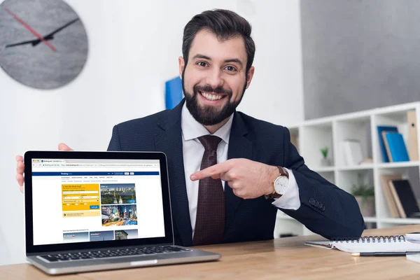 Porträt eines lächelnden Geschäftsmannes, der am Arbeitsplatz im Büro auf den Laptop zeigt — Stockfoto
