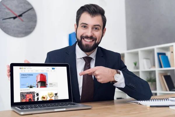 Retrato de empresario alegre apuntando a la computadora portátil en el lugar de trabajo en la oficina — Stock Photo