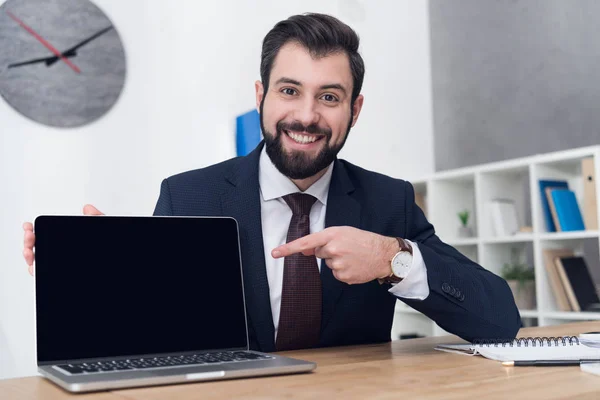 Porträt eines fröhlichen Geschäftsmannes, der am Arbeitsplatz im Büro auf den Laptop zeigt — Stockfoto