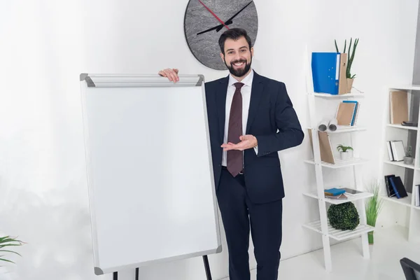 Sonriente hombre de negocios apuntando a la pizarra blanca vacía en la oficina - foto de stock