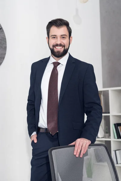 Portrait of cheerful businessman in suit standing at workplace in office — Stock Photo