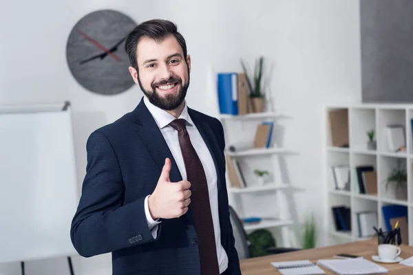 Retrato de un hombre de negocios sonriente mostrando el pulgar hacia arriba en la oficina - foto de stock