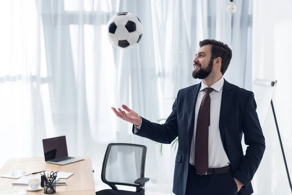 Porträt eines lächelnden Geschäftsmannes, der am Arbeitsplatz im Büro mit Fußball spielt — Stockfoto