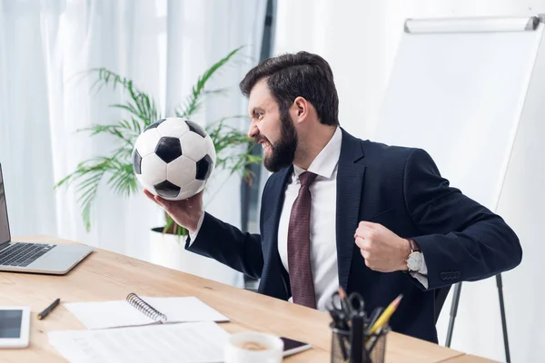 Homme d'affaires en colère en costume avec ballon de football sur le lieu de travail au bureau — Photo de stock