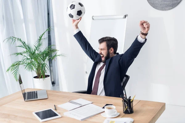 Empresário animado em terno com bola de futebol no local de trabalho no escritório — Fotografia de Stock