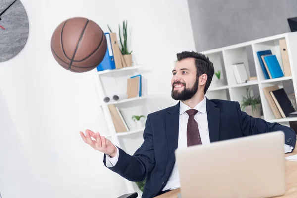 Uomo d'affari sorridente che lancia palla da basket sul posto di lavoro in ufficio — Foto stock