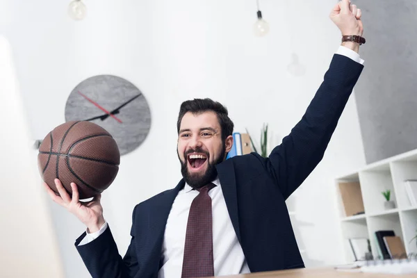 Hombre de negocios emocionado con pelota de baloncesto en el lugar de trabajo en la oficina - foto de stock