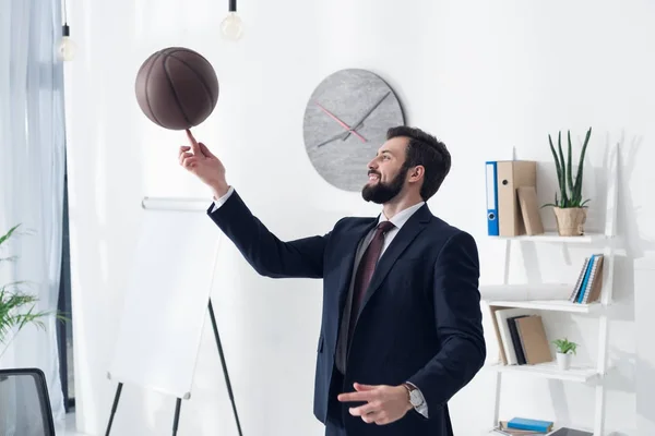 Side view of young businessman in suit playing basketball in office — Stock Photo