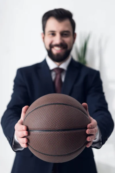 Selective focus of smiling businessman showing basketball ball in hands in office — Stock Photo