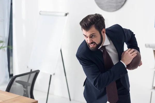 Вид разгневанного бизнесмена в костюме, играющего в регби в офисе — стоковое фото