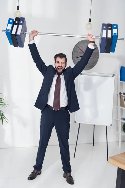 Emotional businessman in suit weightlifting folders in office — Stock Photo