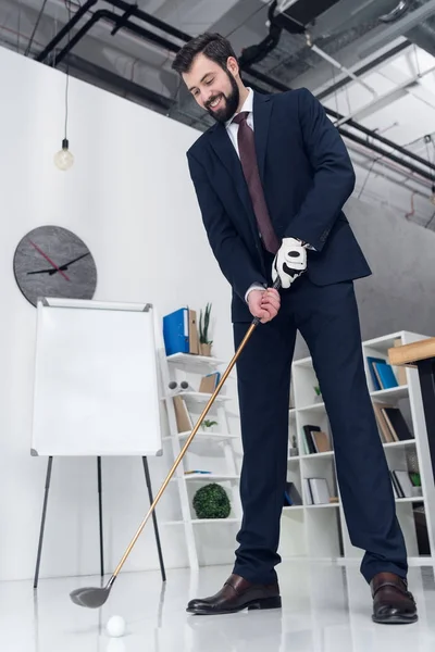 Tiefansicht eines lächelnden Geschäftsmannes im Anzug beim Golfspielen im Büro — Stockfoto