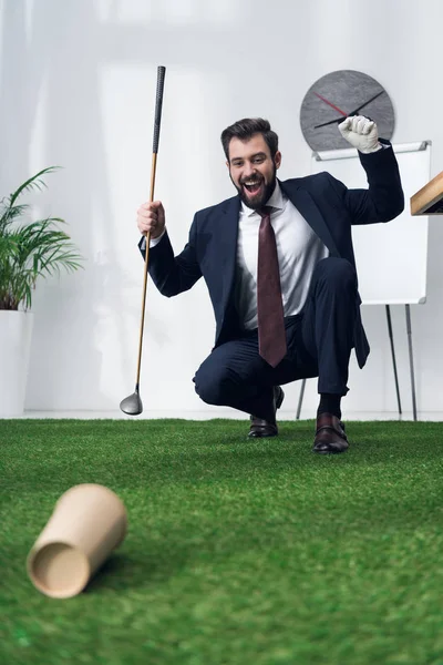 Aufgeregter junger Geschäftsmann spielt Golf im Büro — Stockfoto