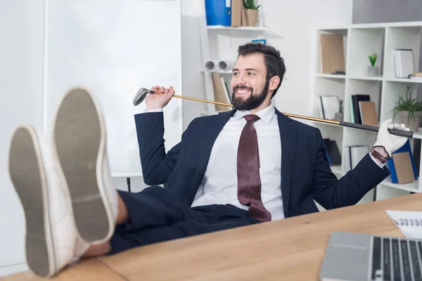 Hombre de negocios sonriente con equipo de golf en el lugar de trabajo en la oficina - foto de stock