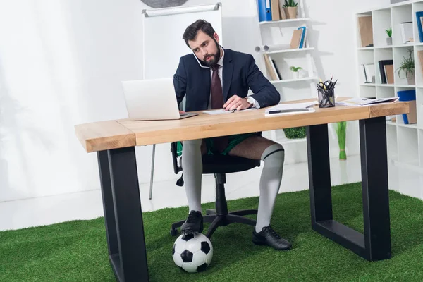 Businessman with soccer ball talking on smartphone at workplace in office — Stock Photo