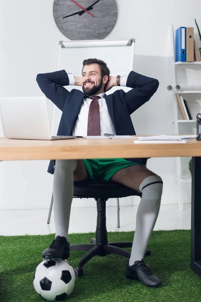 Hombre de negocios feliz con pelota de fútbol descansando en el lugar de trabajo en la oficina - foto de stock
