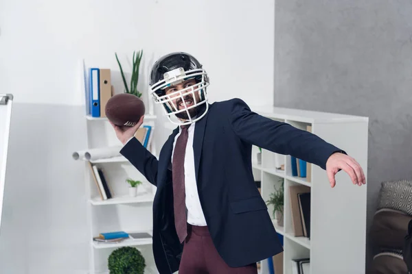 Portrait of young furious businessman in helmet playing rugby in office — Stock Photo