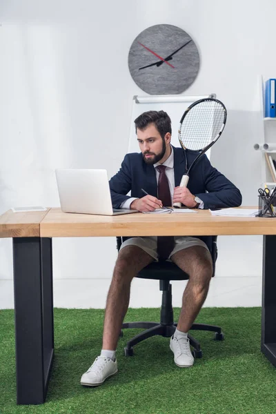 Empresario enfocado con raqueta de tenis trabajando en el lugar de trabajo en la oficina - foto de stock