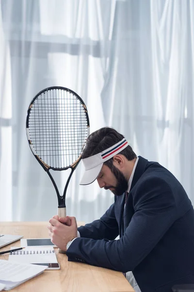 Side view of pensive businessman in suit with tennis racket at workplace — Stock Photo