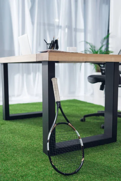 Vue rapprochée du lieu de travail avec ordinateur portable et raquette de tennis au bureau — Photo de stock