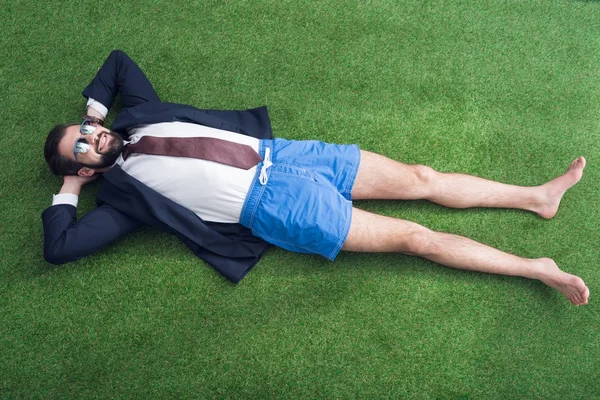 Vista aérea del hombre de negocios en chaqueta y pantalones cortos descansando sobre césped verde - foto de stock