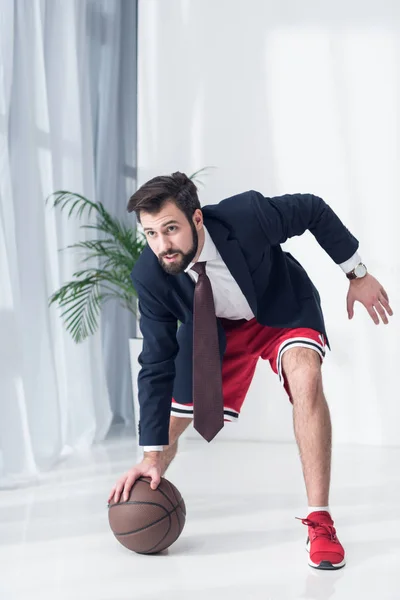 Businessman in jacket and shorts playing basketball in office — Stock Photo