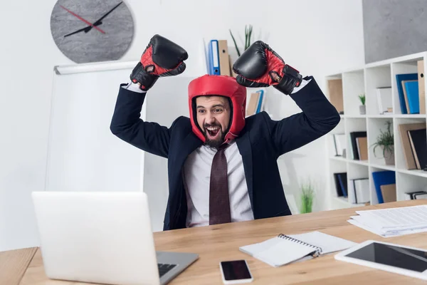 Retrato de empresario excitado en guantes de boxeo y casco en el lugar de trabajo en la oficina - foto de stock