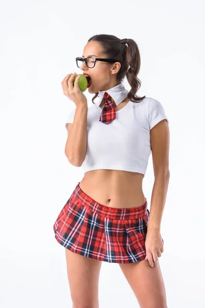 Joven sexy colegiala en corto rojo falda a cuadros comer manzana aislado en blanco - foto de stock