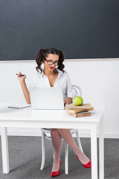 Joven sexy profesor sentado en el escritorio con el ordenador portátil - foto de stock