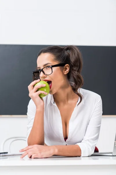 Giovane insegnante sexy mangiare mela alla scrivania in classe — Foto stock