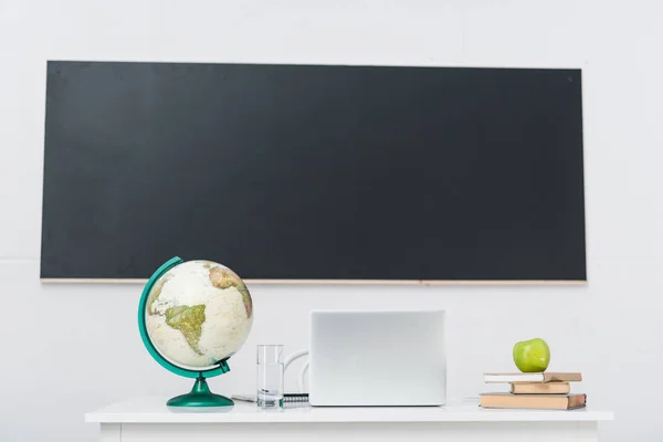 Teachers desk with laptop in classroom in front of chalkboard — Stock Photo