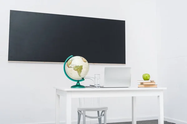 Teachers desk in classroom in front of chalkboard — Stock Photo