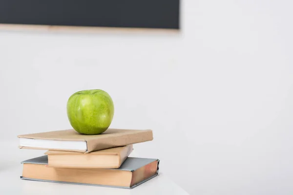 Manzana verde en libros apilados en el aula - foto de stock