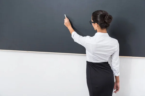 Hermosa joven profesor escribiendo con tiza en pizarra - foto de stock