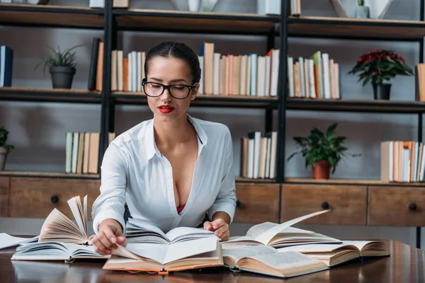 Giovane insegnante sexy seduto in biblioteca e lettura — Foto stock