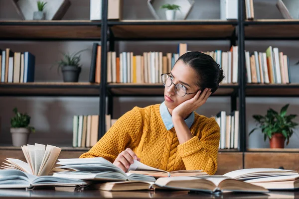Thoughtful young student girl looking away while sitting at library — Stock Photo
