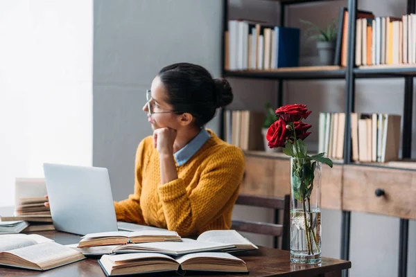 Young student girl preparing for exam at library with red roses in vase — Stock Photo