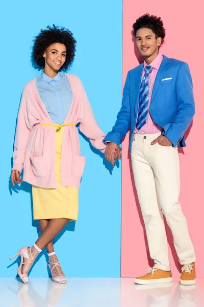 Young african amercian smiling girl and guy holding hands on pink and blue background — Stock Photo